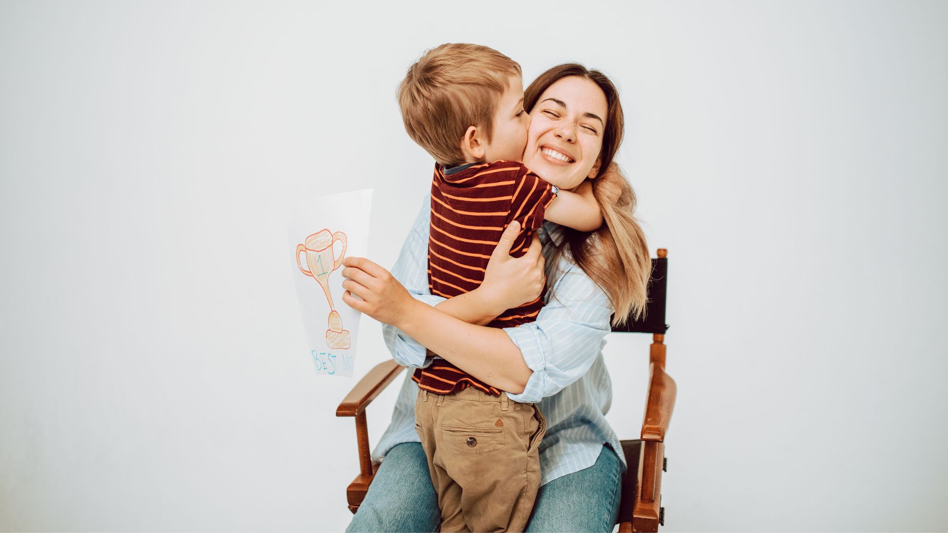 Imagem de uma mãe, segurando um desenho e abraçando seu filho, que está beijando seu rosto