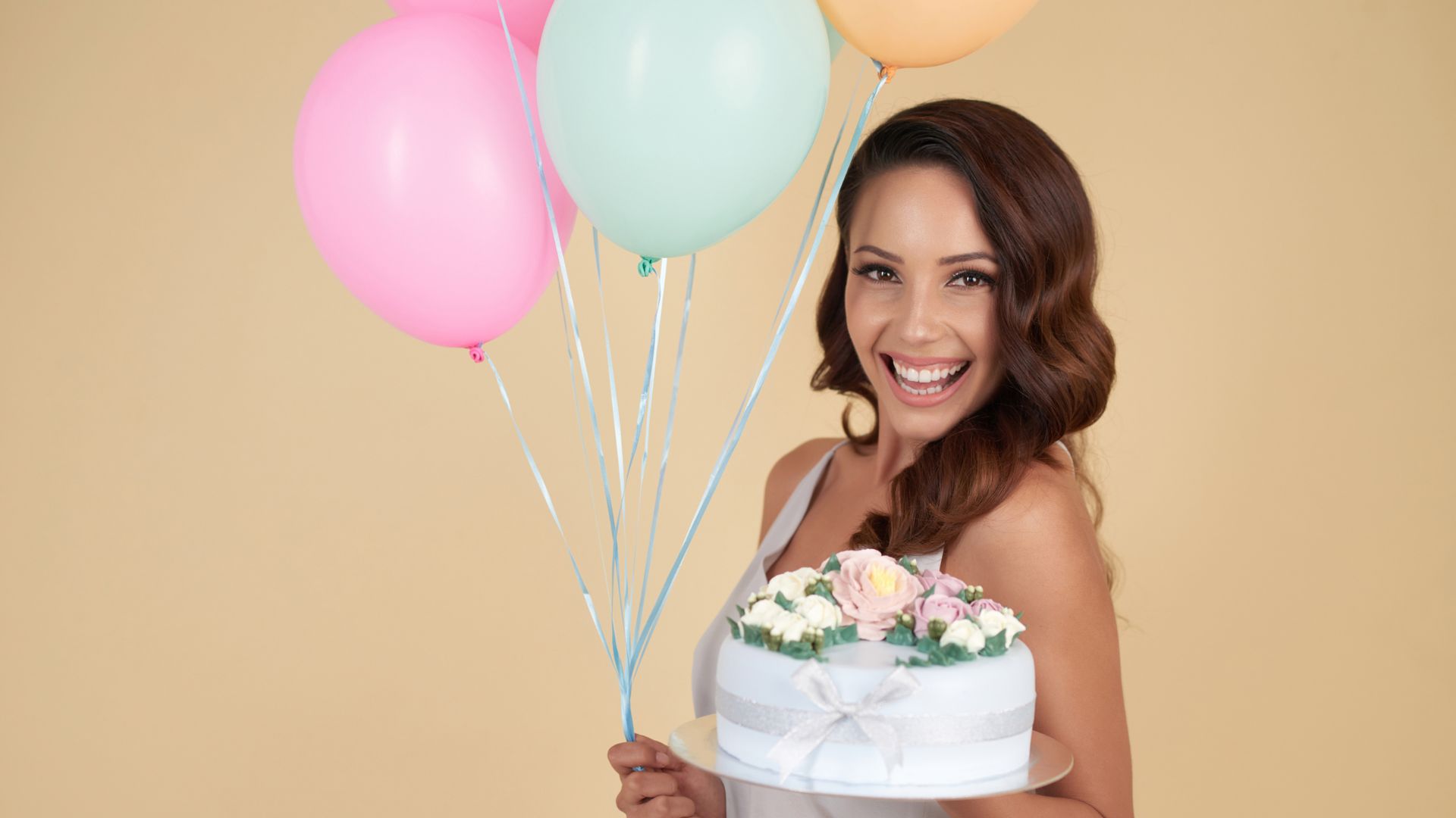 Imagem de uma moça sorrindo, segurando um bolo de aniversário e balões