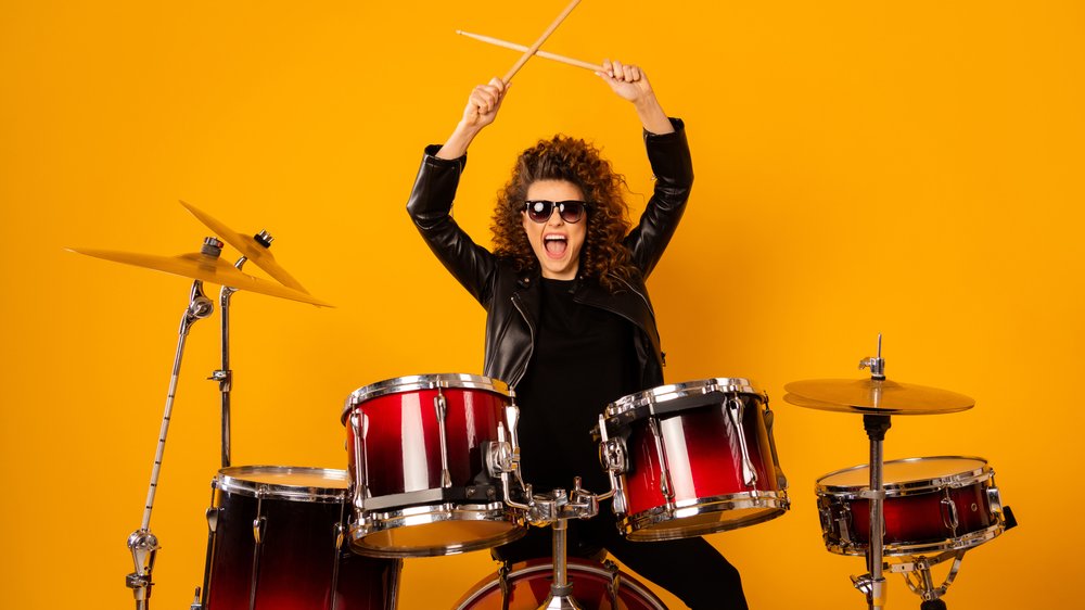 Roman Samborskyi / Shutterstock Mulher branca de cabelos cacheados e escuros tocando bateria.