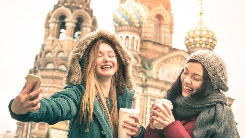 Duas amigas com café na mão tirando uma foto em frente a uma igreja