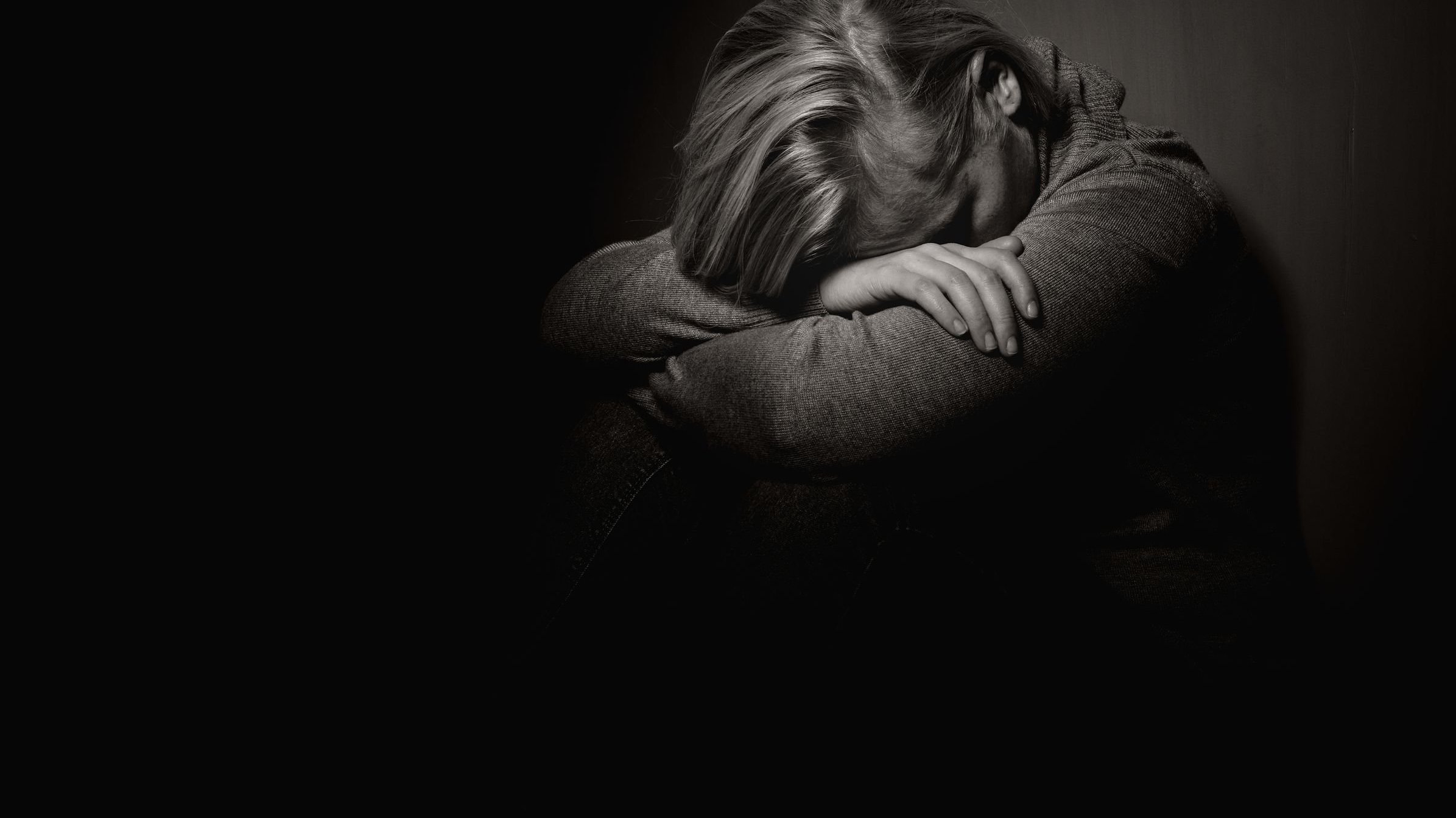 Mulher sentada no chão em um ambiente escuro com seu rosto entre os braços