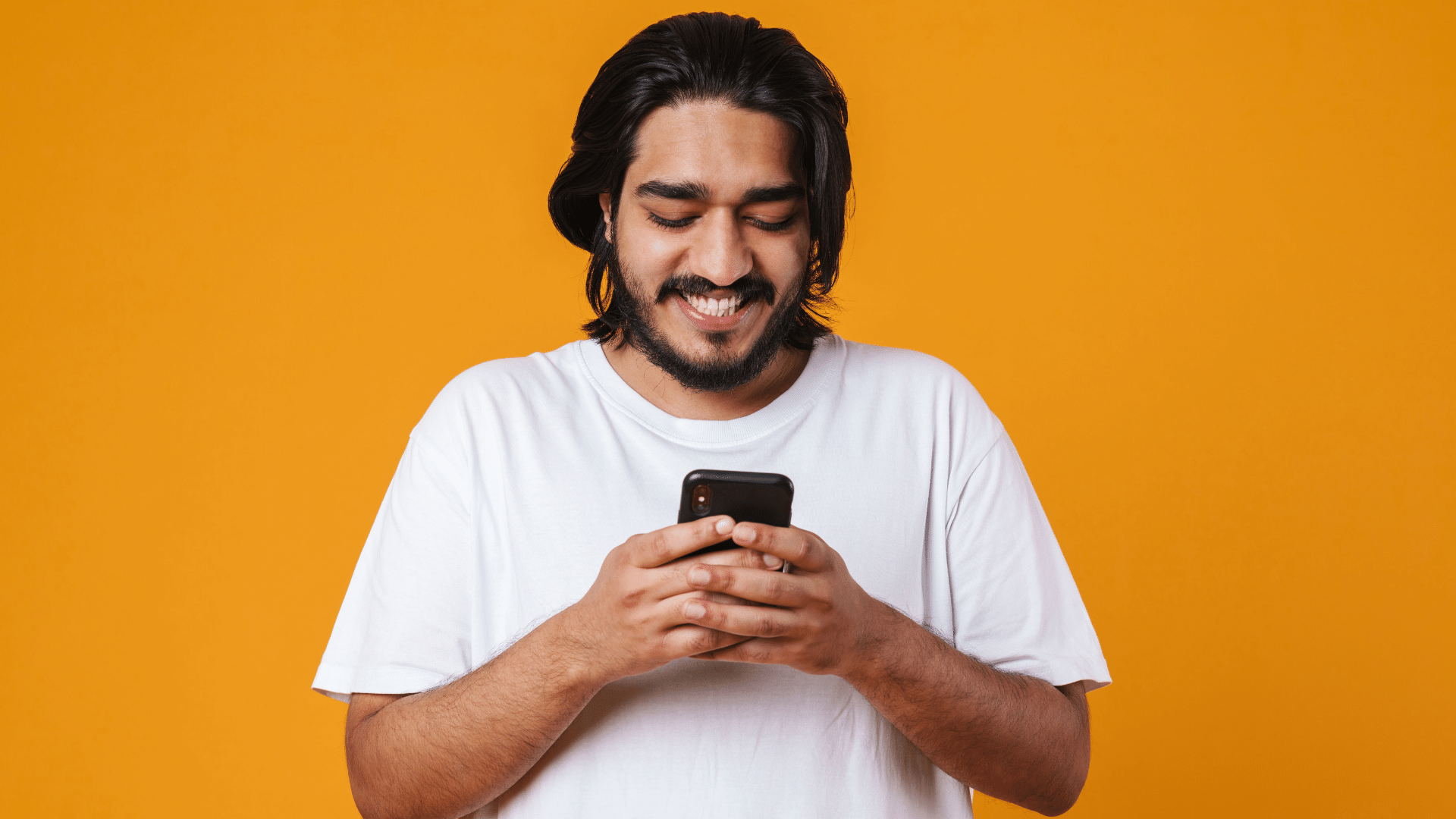 Foto de um homem sorrindo em um fundo amarelo, olhando para o celular.