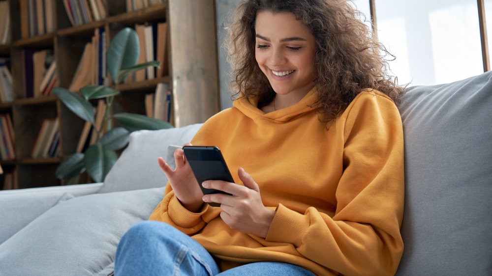 Ground Picture / Shutterstock.com Mulher sorrindo enquanto olha para o celular