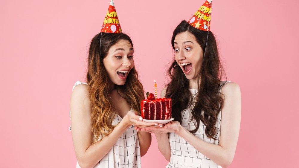 Duas amigas felizes olhando para o bolo de aniversário e vestindo chapéus de aniversário.