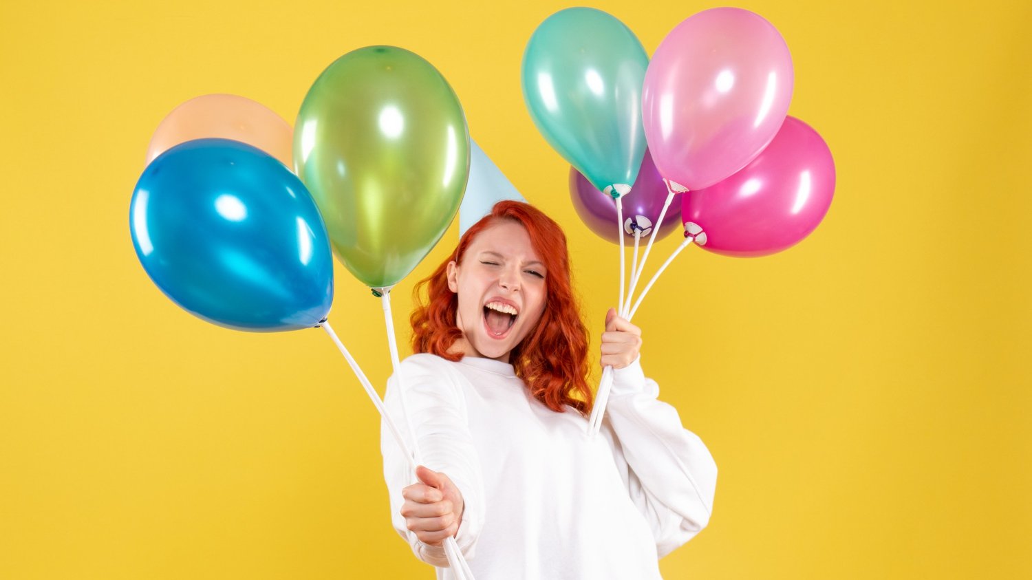 Mulher branca com cabelos ruivos sorrindo e segurando vários balões de festa