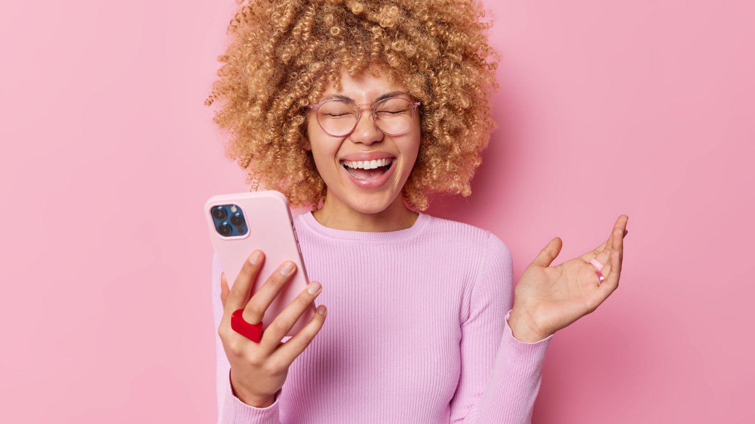 Mulher negra com o celular na mão dando risada