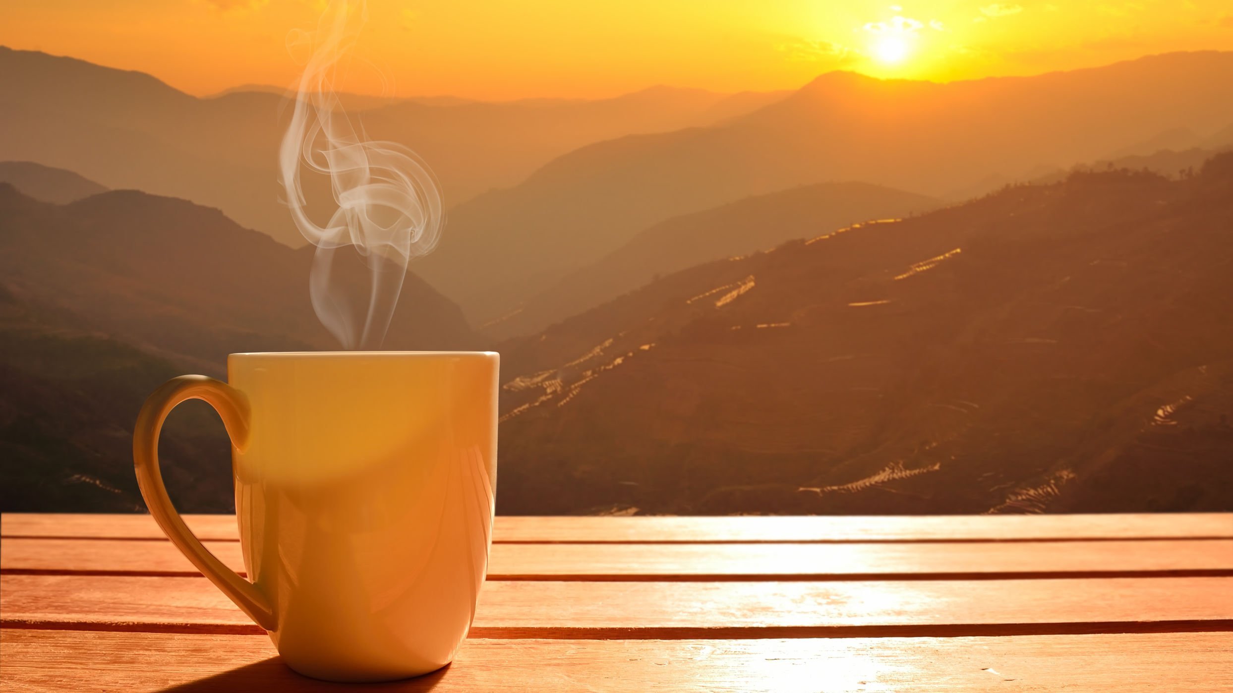 Xícara de café uma mesa e ao fundo montanhas com o sol nascendo
