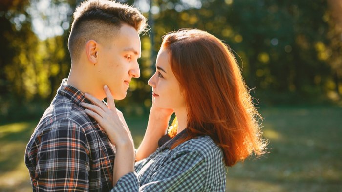 Casal de homem e mulher se olhando apaixonados, tocando o rosto um do outro com as mãos, em um dia ensolarado.