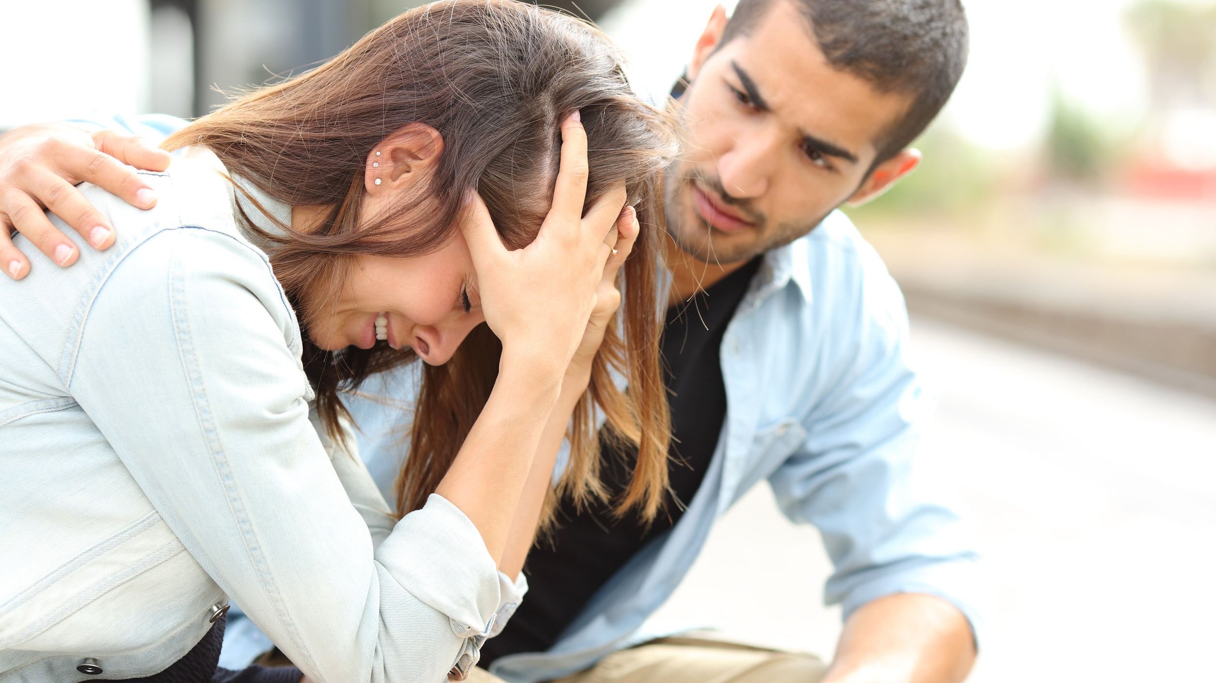 Mulher chorando com mãos na cabeça e homem tentando consolar