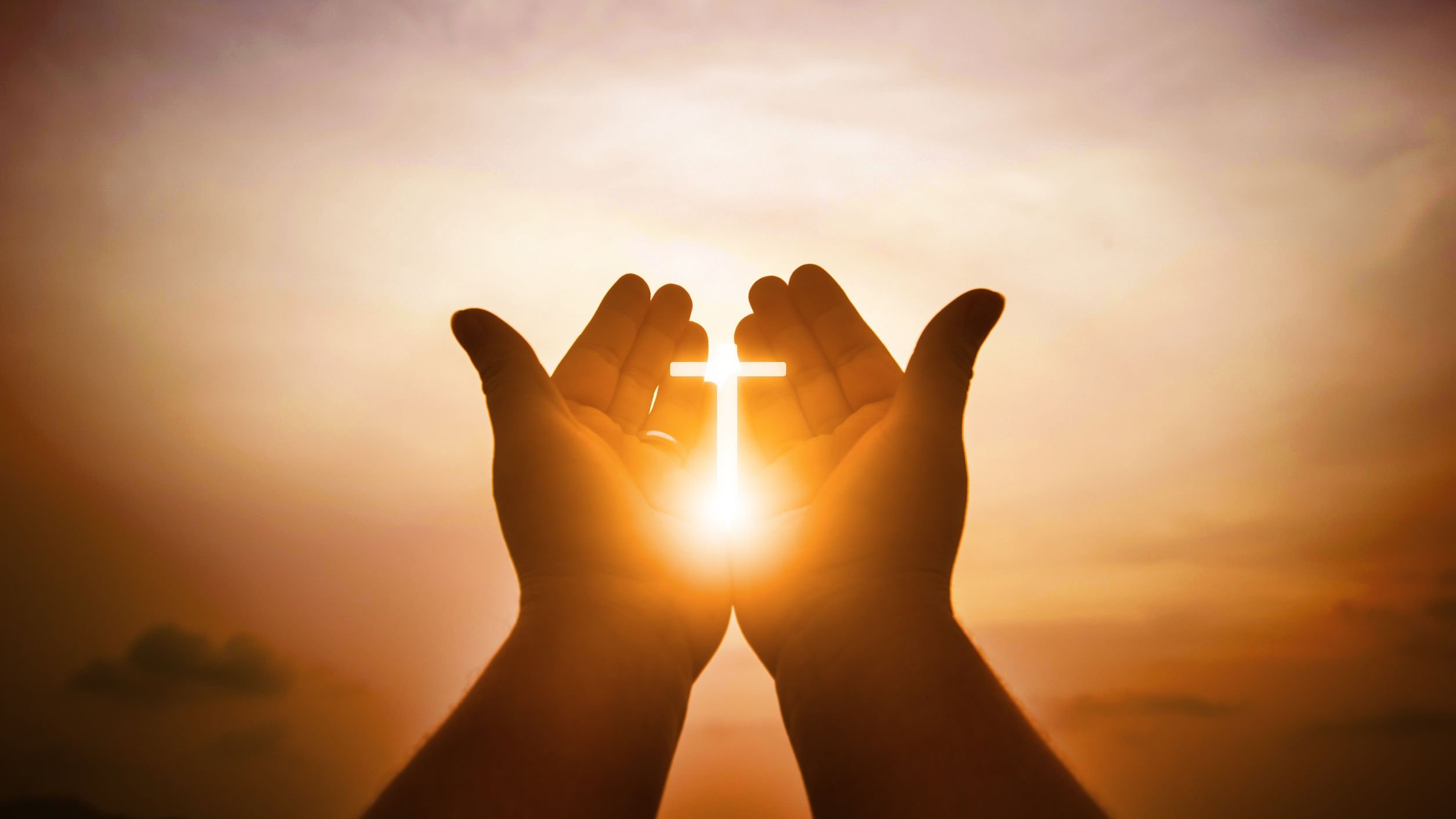 Cruz iluminada entre as mãos de uma pessoa, ao pôr do sol
