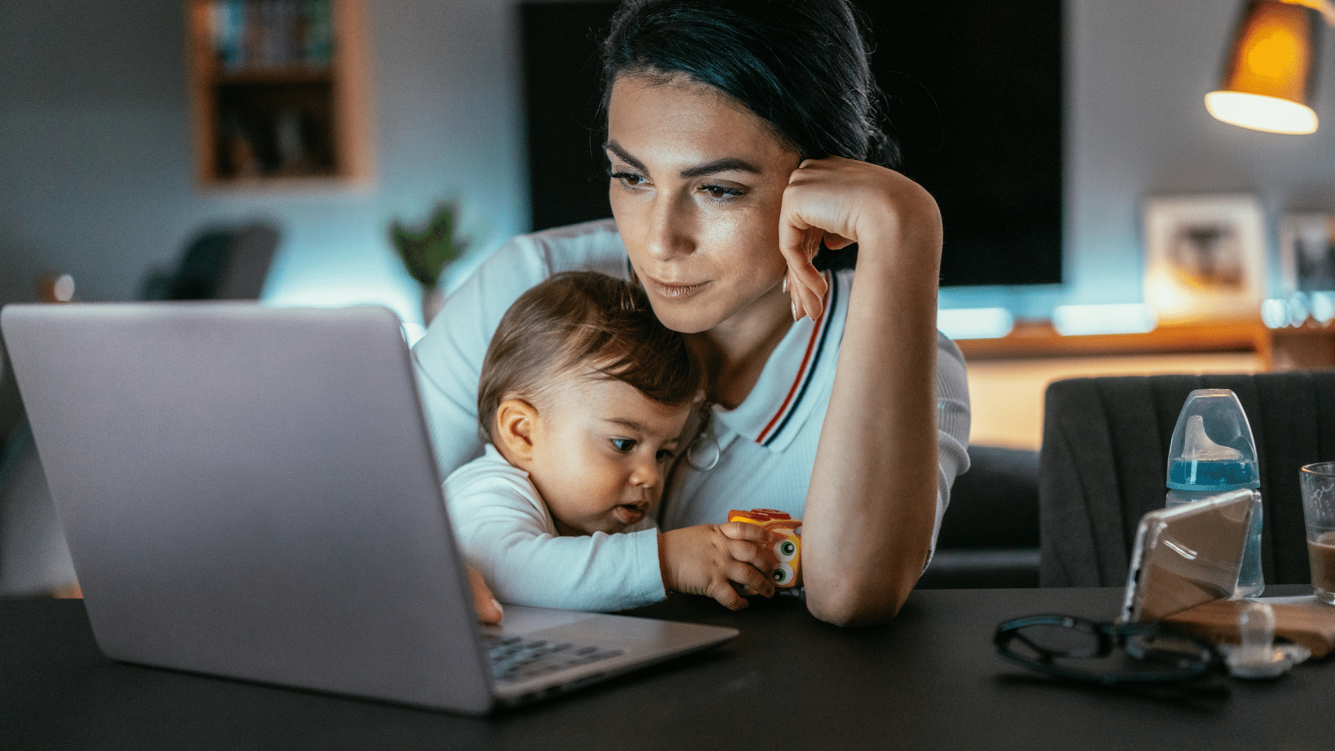 Imagem de uma mãe segurando o seu bebê no colo na frente de um laptop