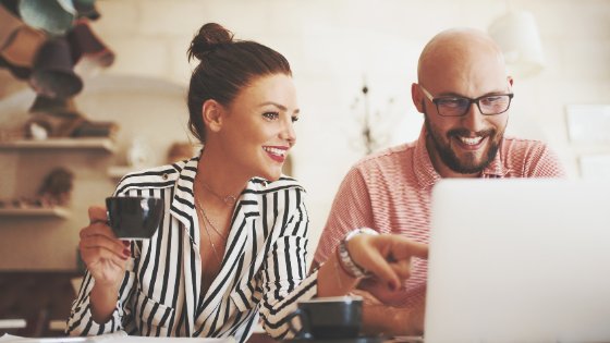 Duas pessoas sorrindo em frente a um computador