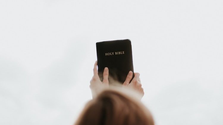 Pessoa erguendo uma bíblia para os céus