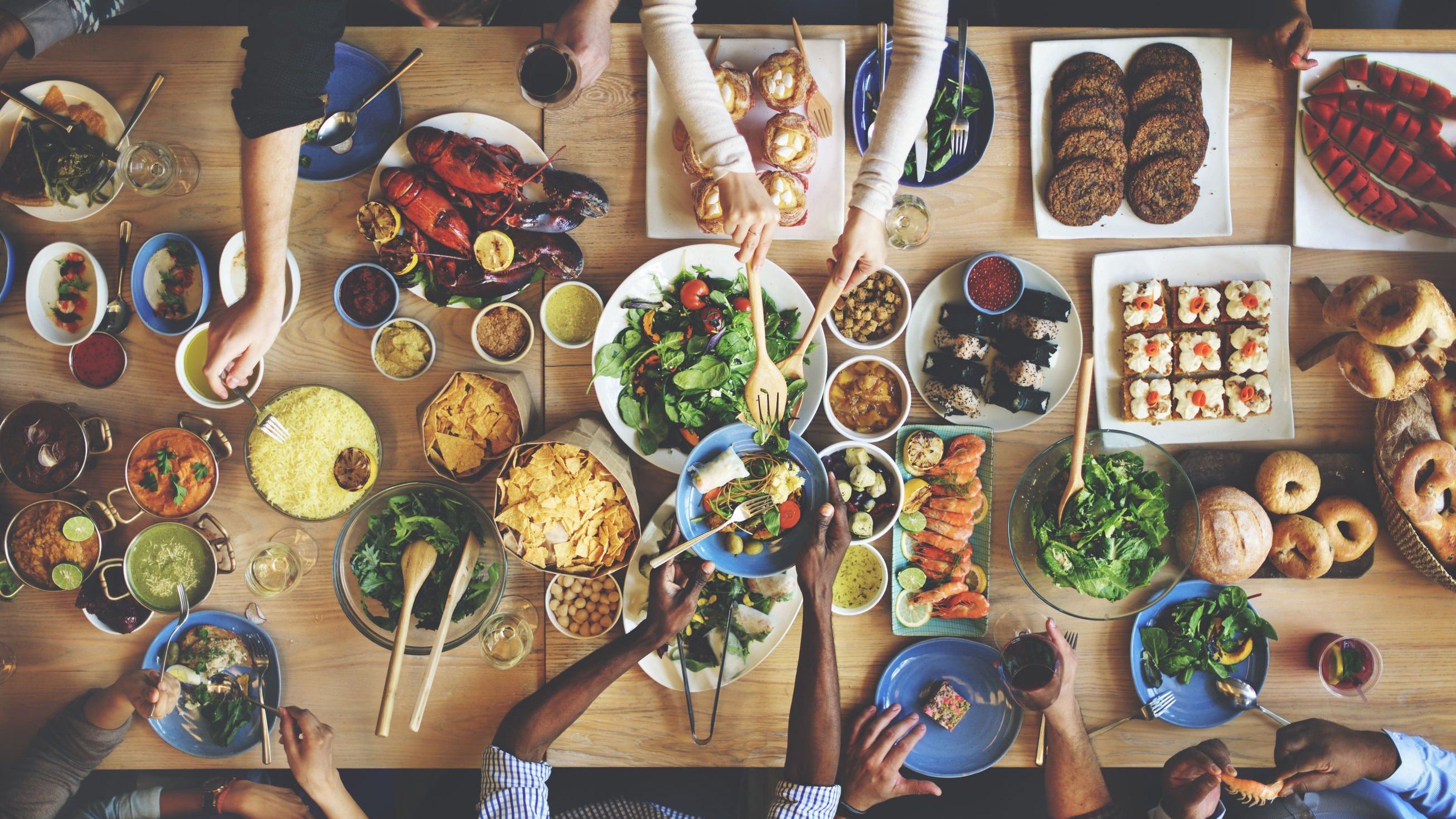 Mesa com comidas vista do alto com mãos pegando alimentos