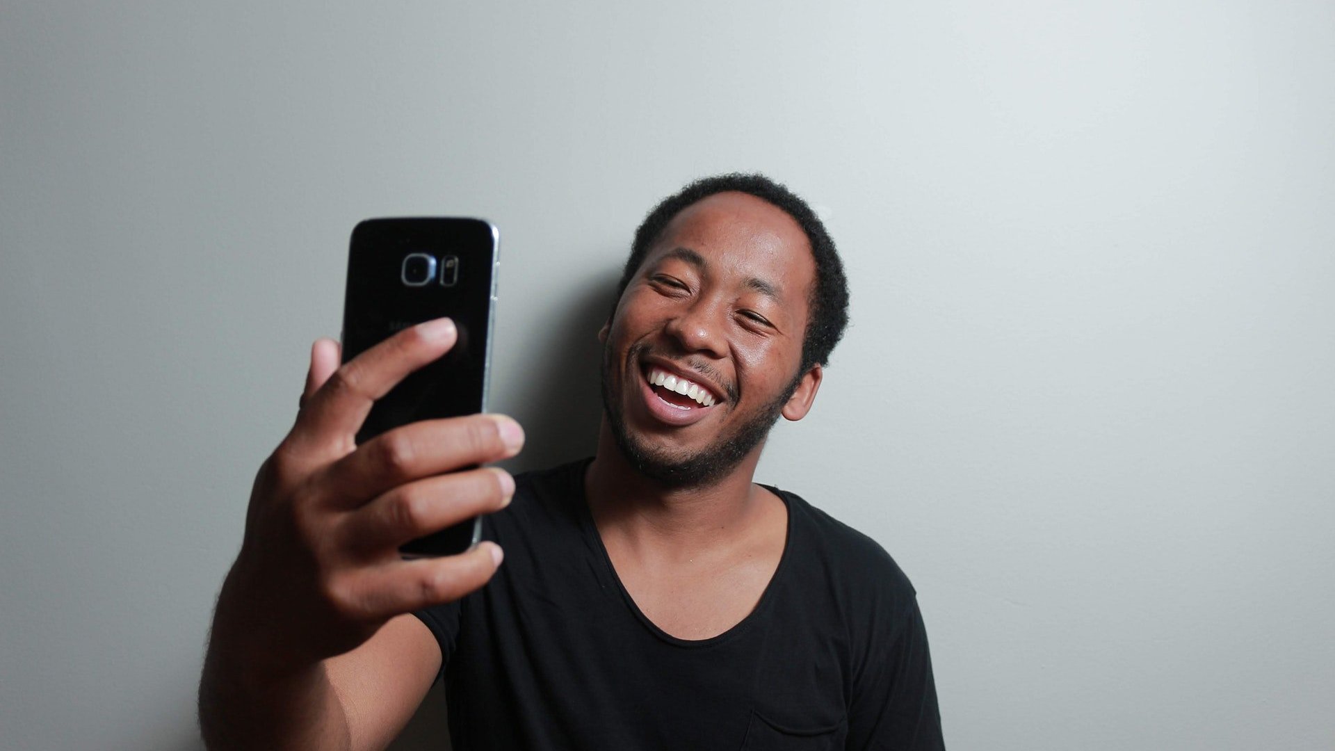 Homem em frente a parede branca sorrindo para uma selfie