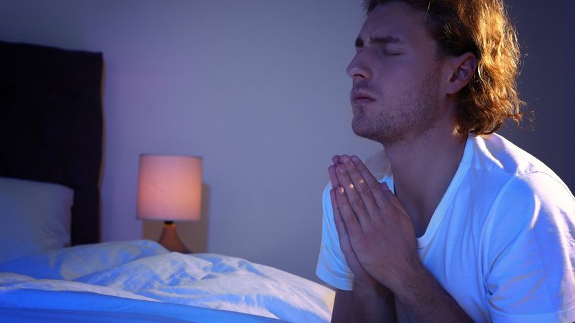 Homem com as mão juntas, rezando na beira da cama