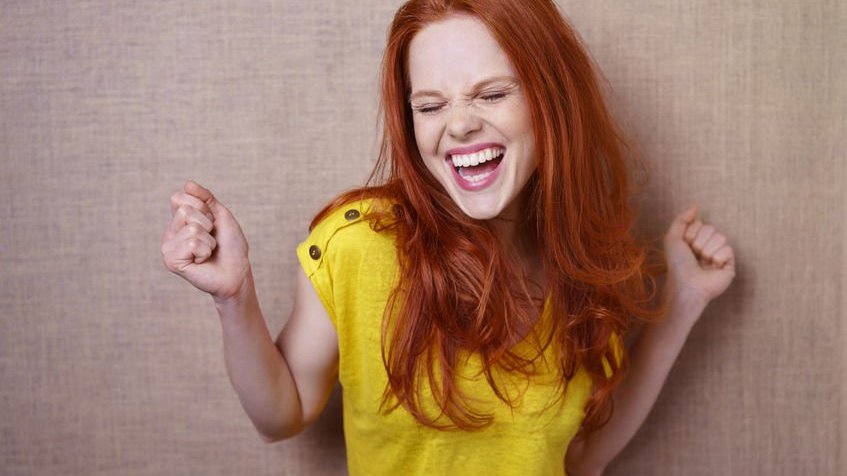 Mulher com expressão feliz de olhos fechados e boca aberta usando blusa amarela