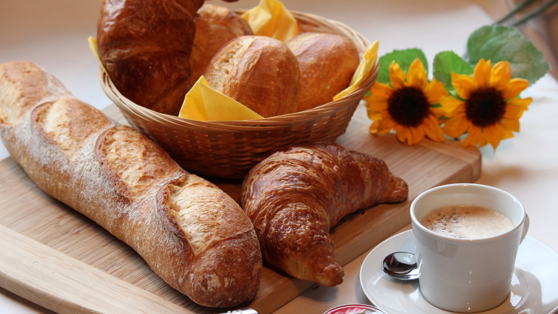 Prato de café da manhã com pães, xícara de café e flor de girassol