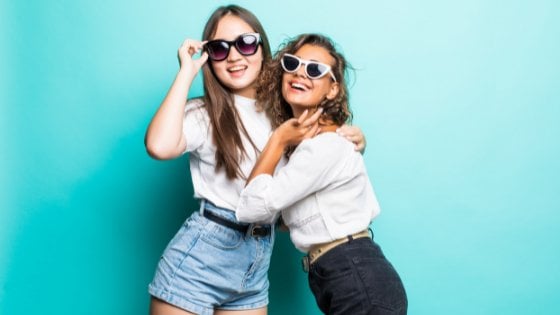 Duas jovens abraçadas sorrindo e usando óculos escuros.