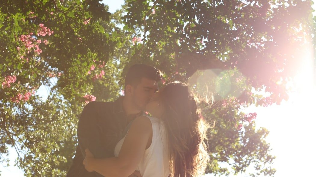Casal se beijando embaixo de uma árvore.