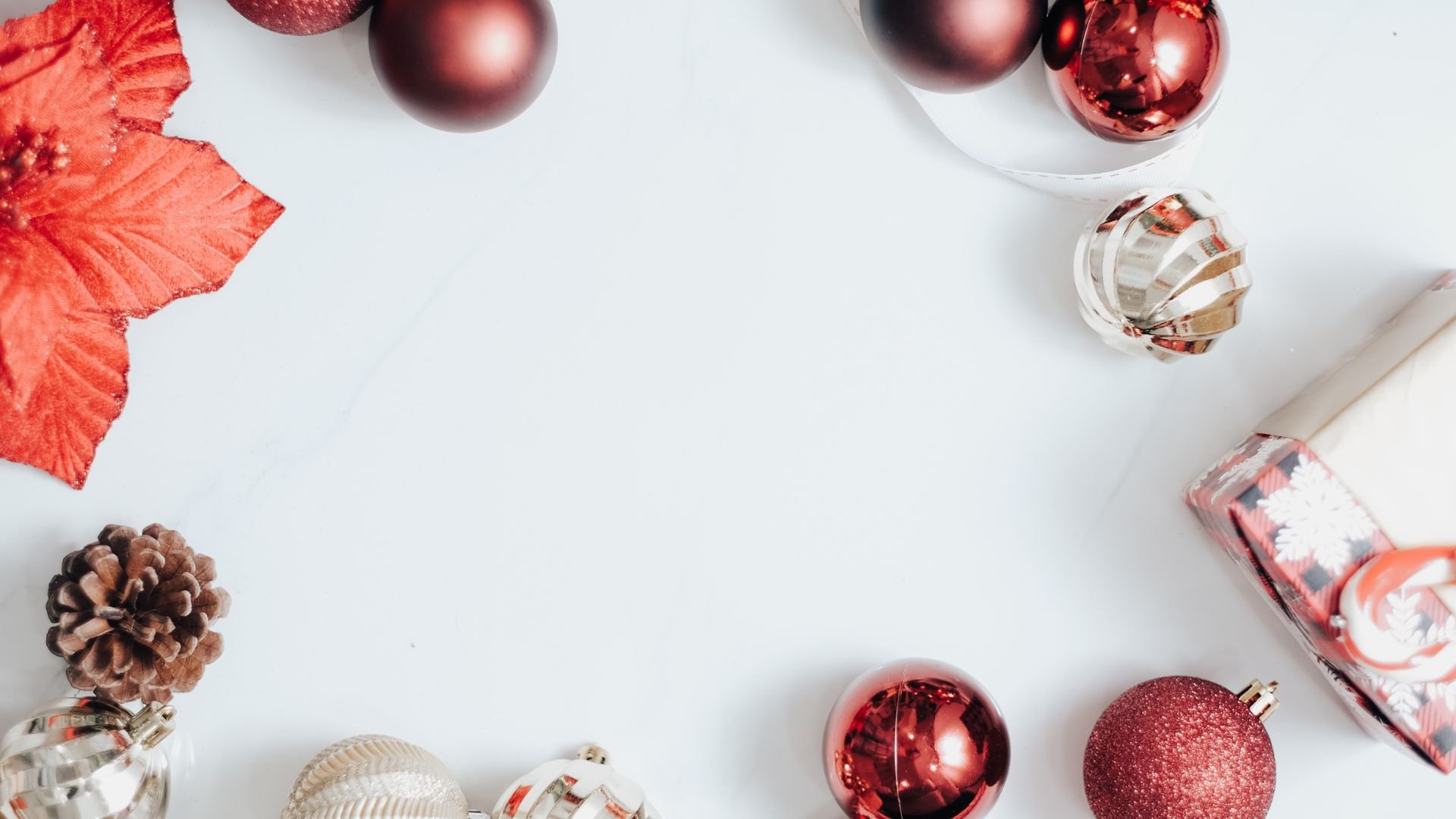 Imagem de fundo branco, com uma moldura feita de elementos natalinos como: flor e bolas vermelhas e douradas, pinhas e caixa de presente.