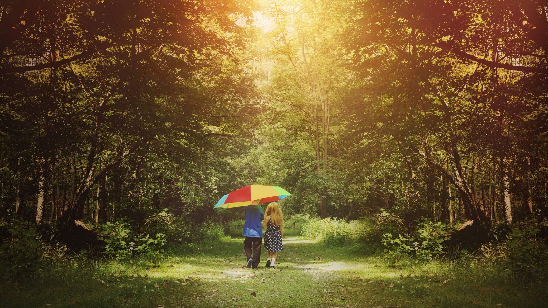 duas crianças andando juntas de guarda chuva pelo campo