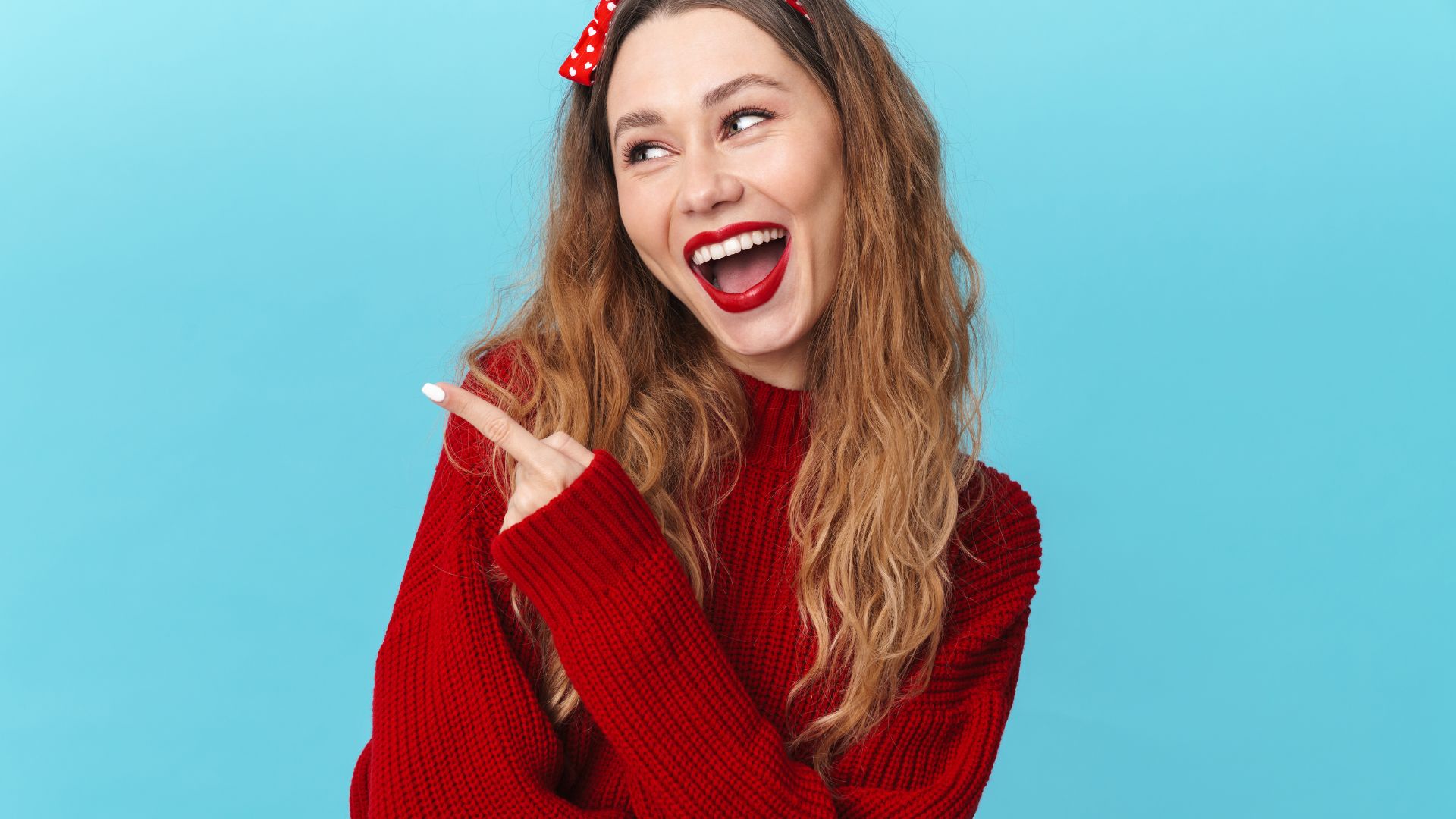 Imagem de fundo azul e em destaque uma mulher de cabelos longos. Ela usa uma blusa de lã, fita no cabelo e batom, todos na cor vermelho.