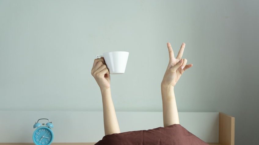 Mãos erguidas com xícara na cama