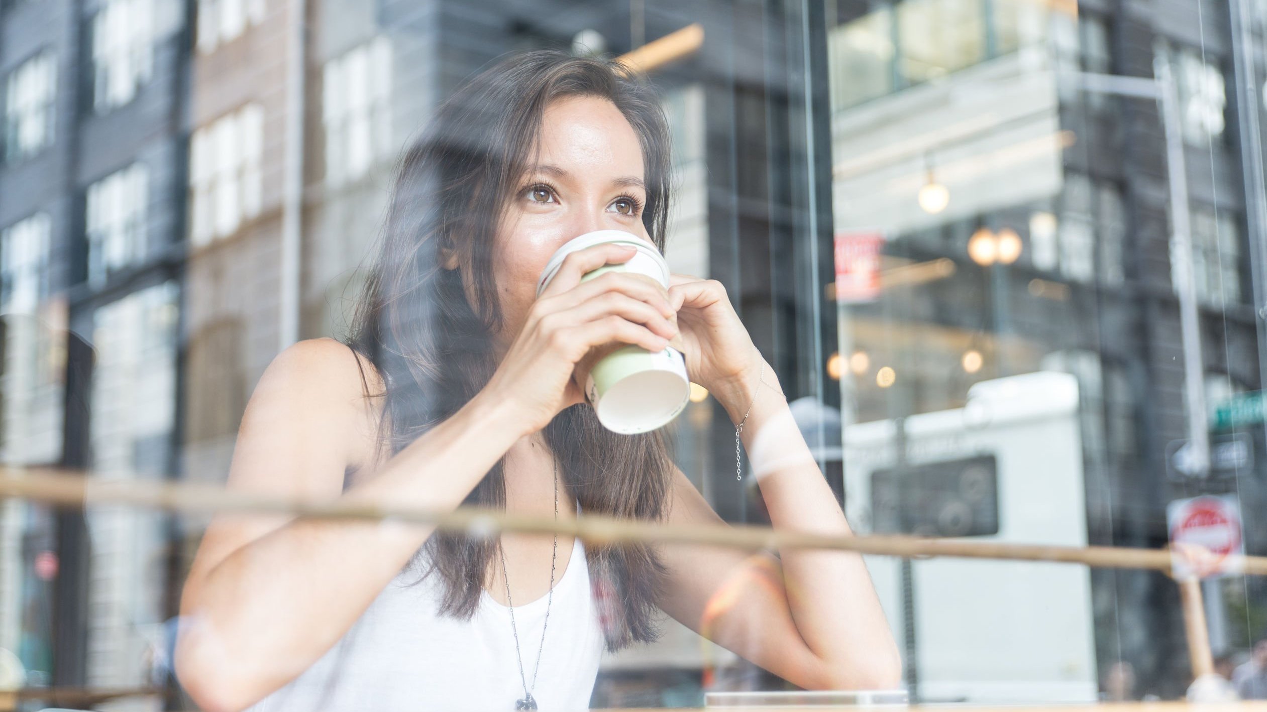 Mulher branca sentada dentro de uma loja tomando café