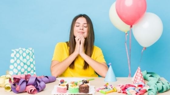 Mulher sentada à mesa de aniversário orando de olhos fechados.