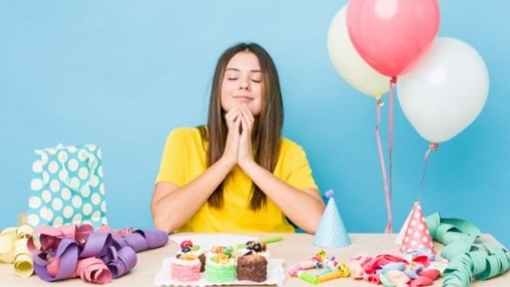 Mulher sentada à mesa de aniversário orando de olhos fechados.