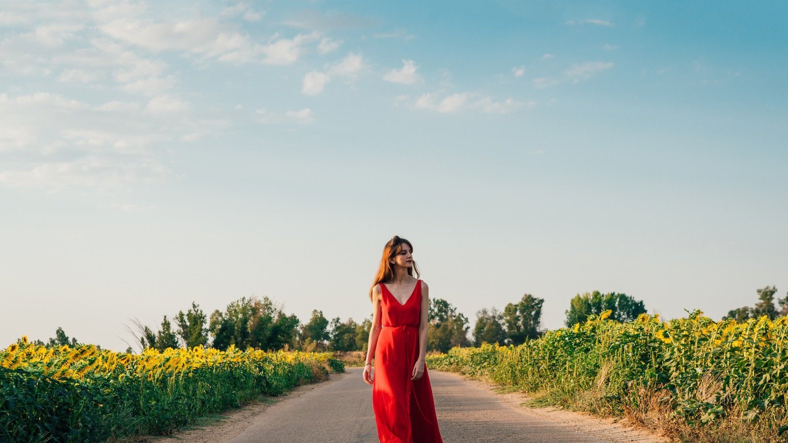 Mulher branca usando vestido vermelho enquanto caminha numa estrada.