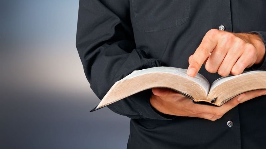 Pastor segurando uma bíblia, enquanto com um dos dedos acompanha a leitura da mesma