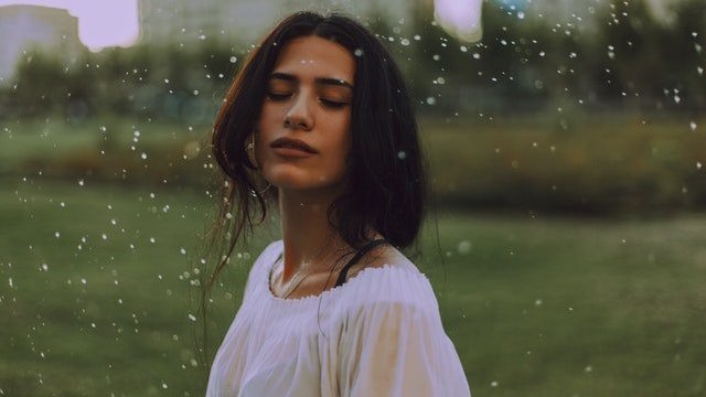 Mulher branca de olhos fechados tomando chuva.