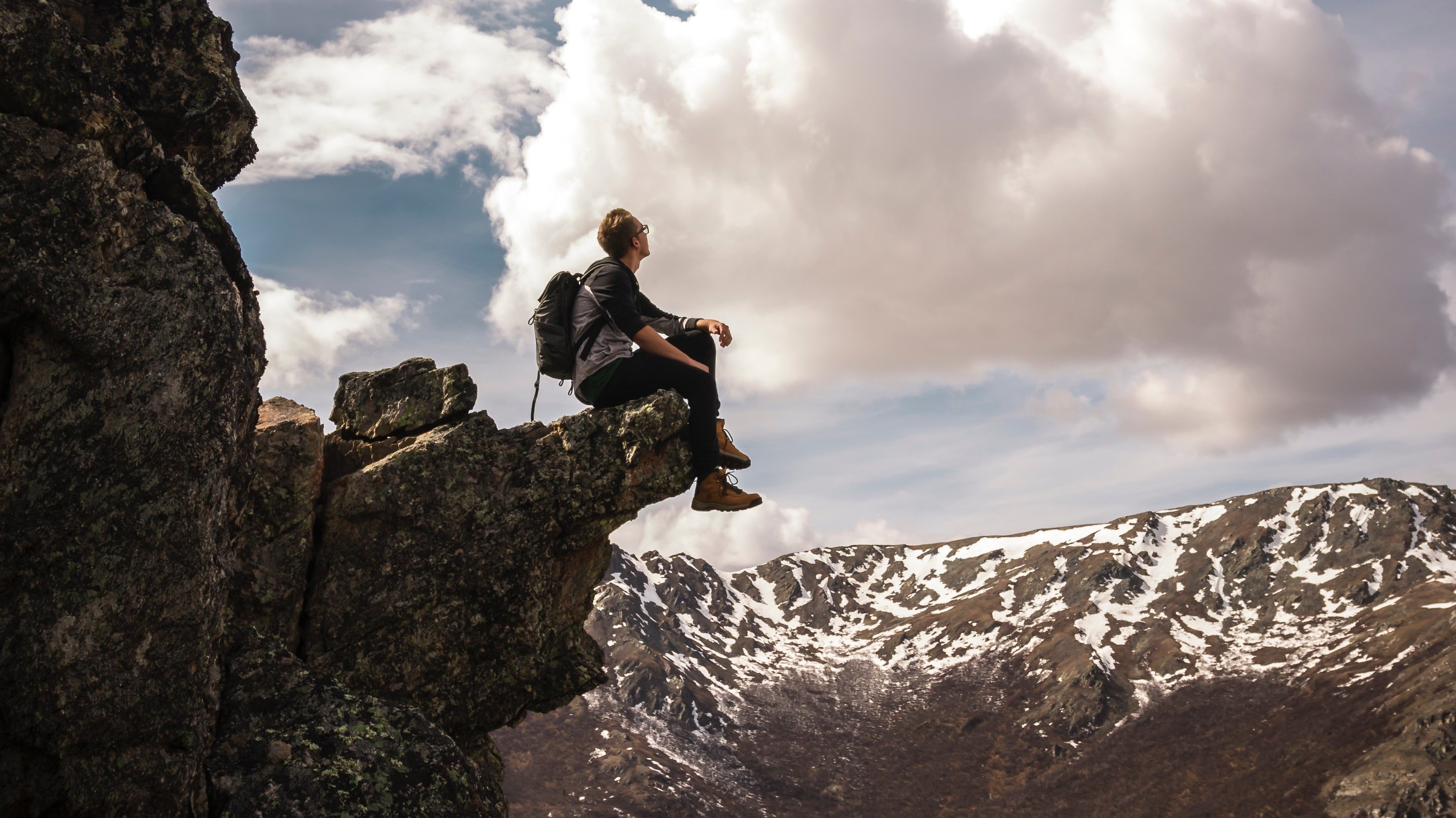 Homem sentado na beira da montanha olhando para o céu