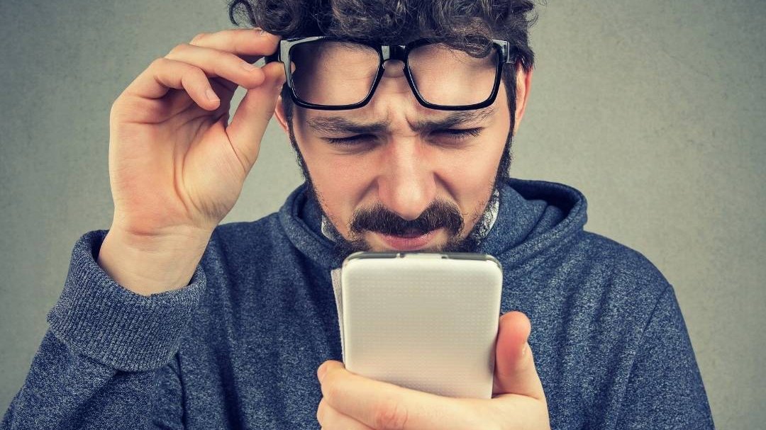 Homem olha para o celular com os óculos levantados.