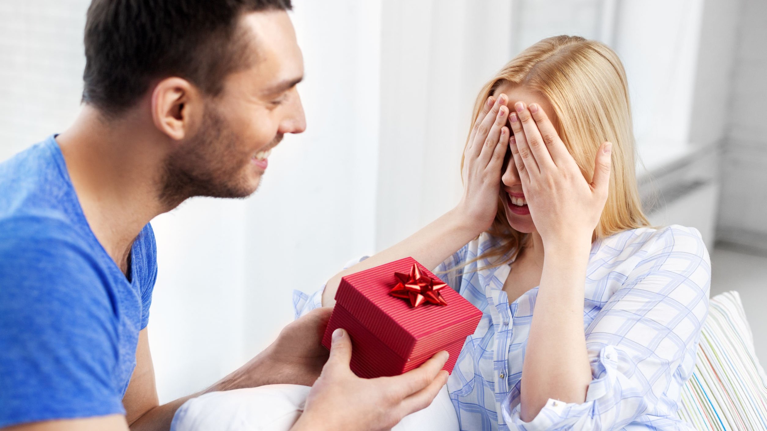 Homem entrega caixa de presente para mulher que cobre os olhos com as mãos.