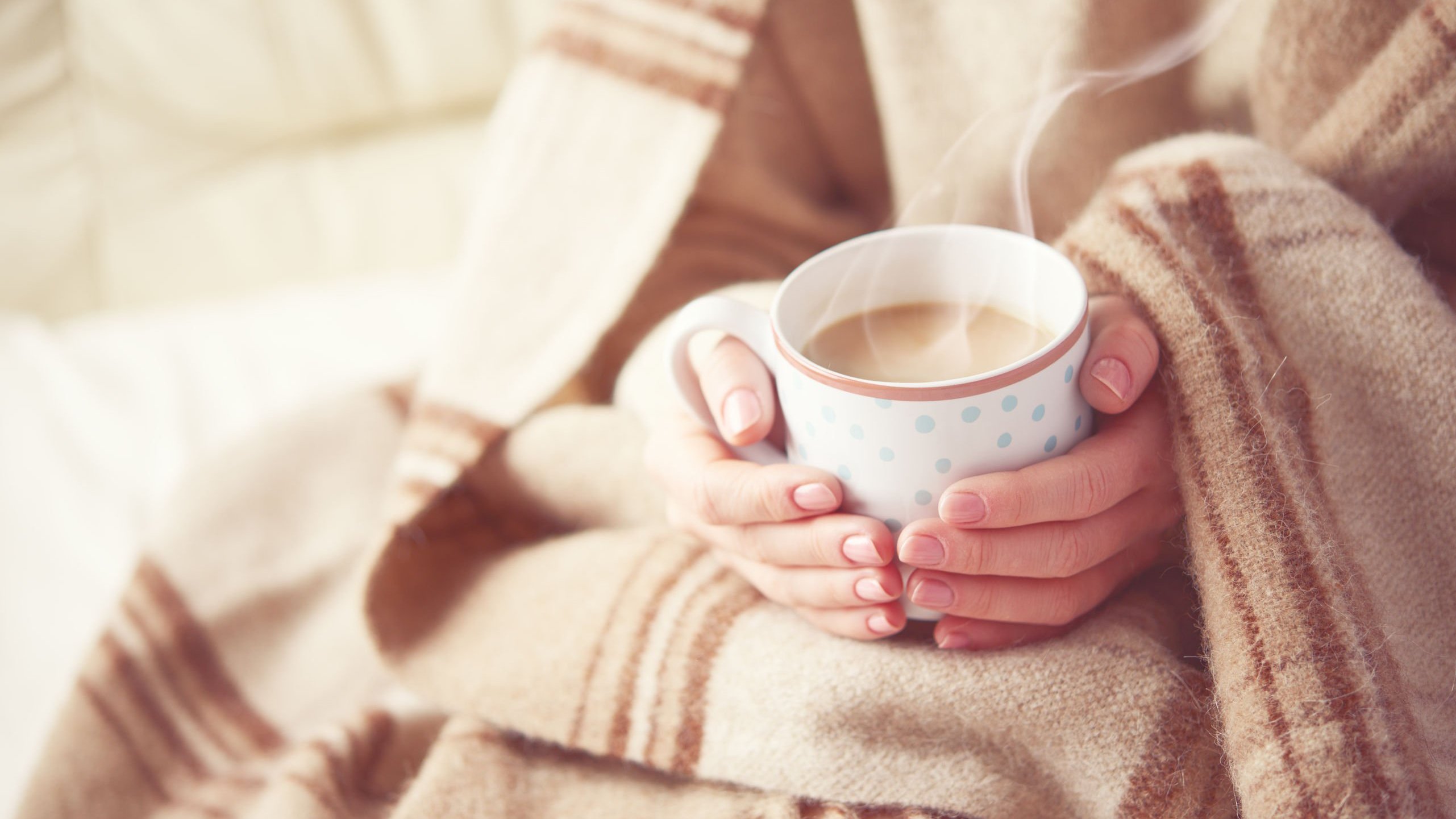 Pessoa com coberta marrom segura xícara com café com leite quente.