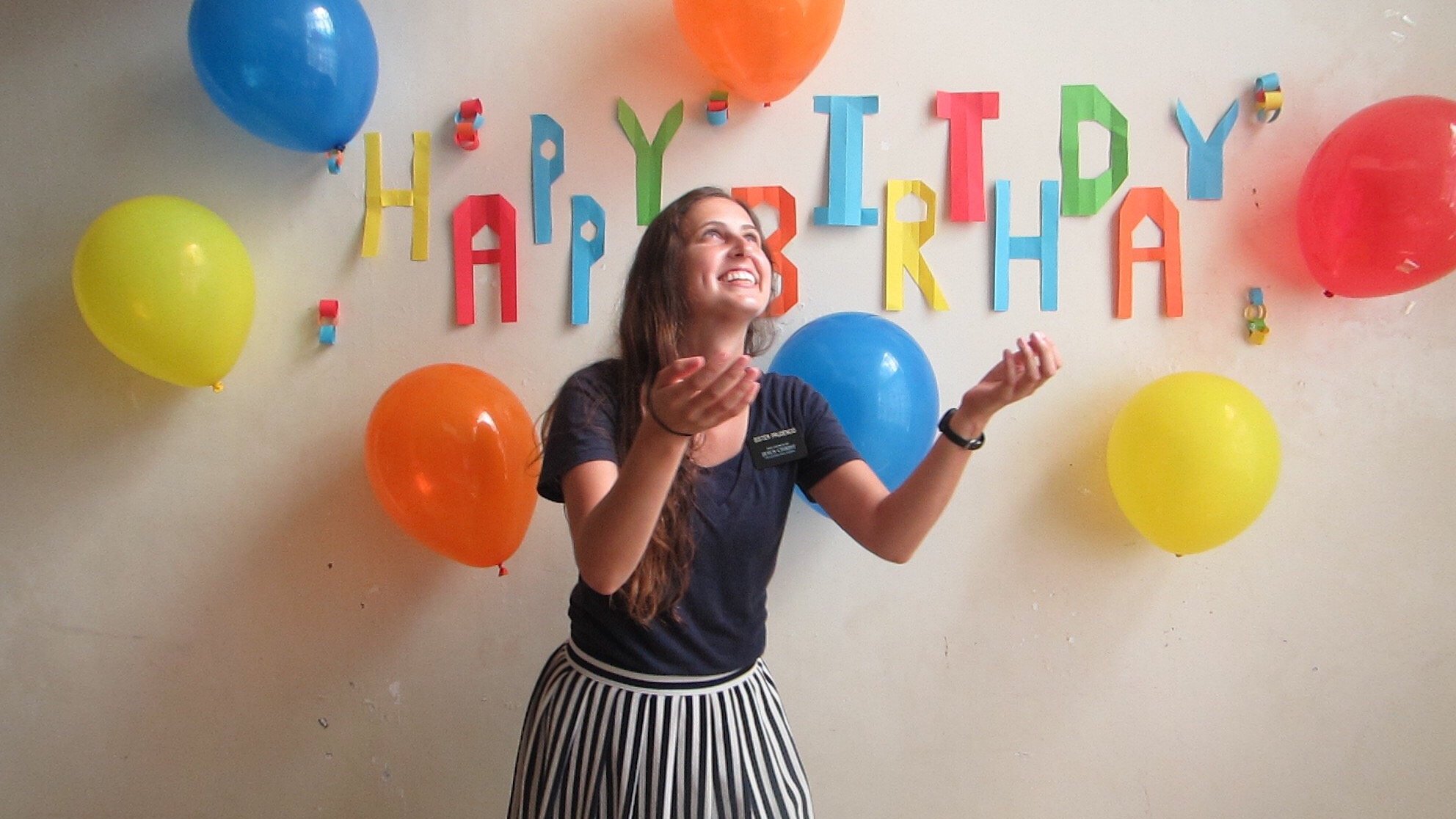 Mulher sorrindo com decoração atrás de balões de aniversário