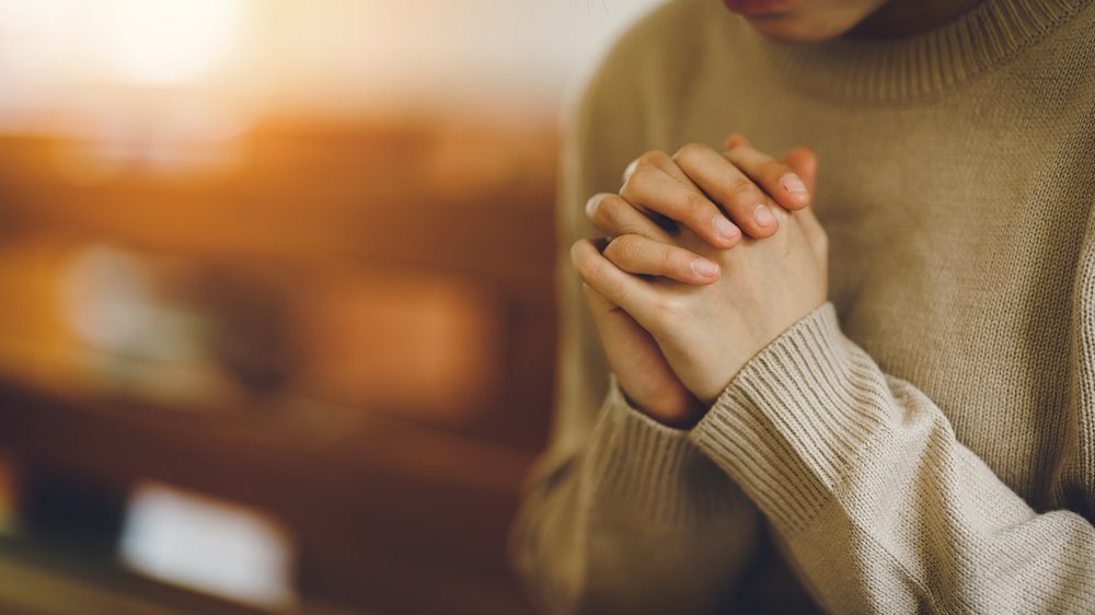 Pessoa com mãos entrelaçadas rezando