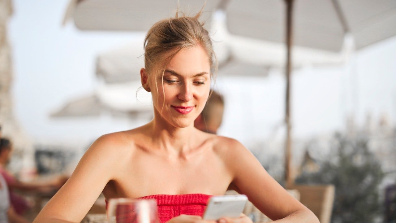 Mulher loira usando o celular em um restaurante ao ar livre.