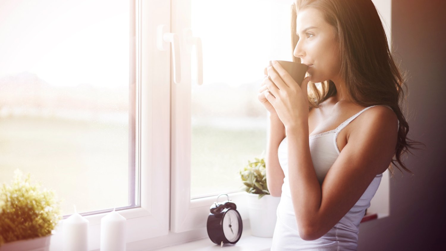 Mulher olhando na janela enquanto toma café