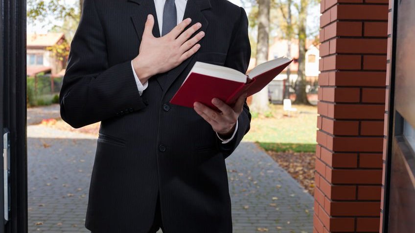 Jovem vestindo terno e gravata, com a mão direita no peito, e a mão esquerda segurando uma bíblia aberta.