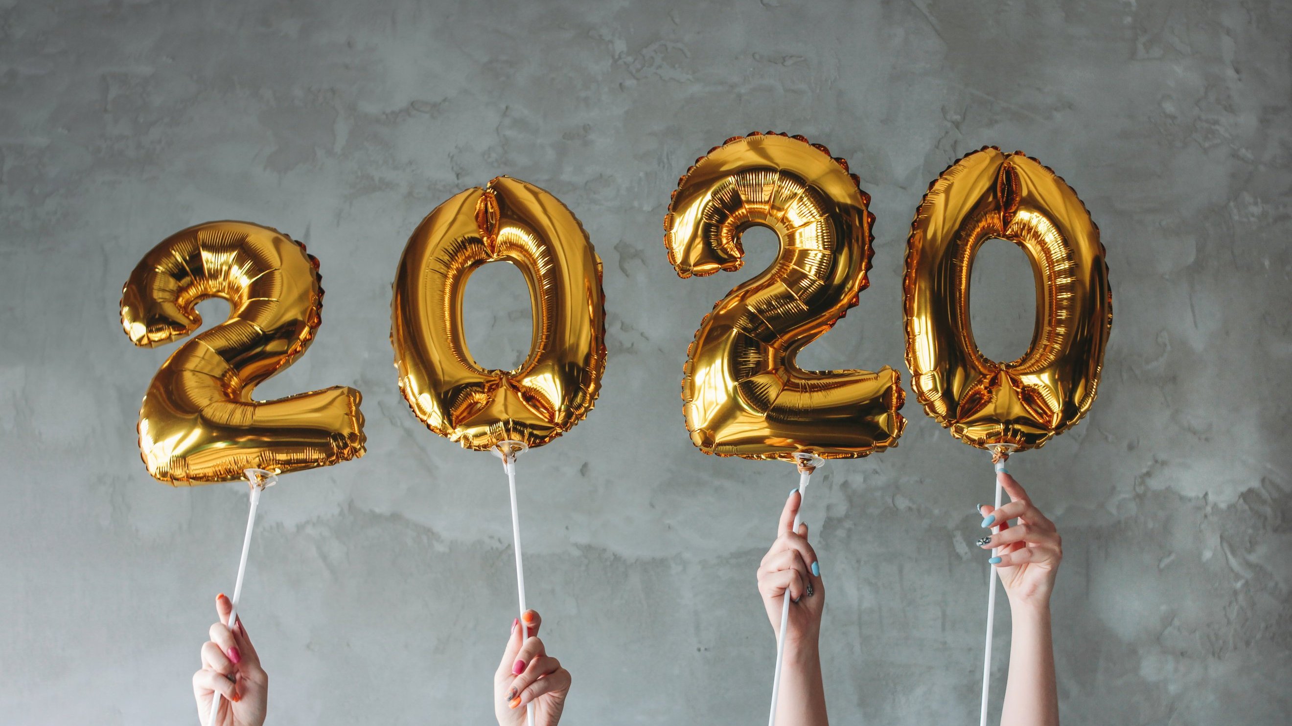 Mãos femininas segurando balões dourados com números que formam o ano 2020