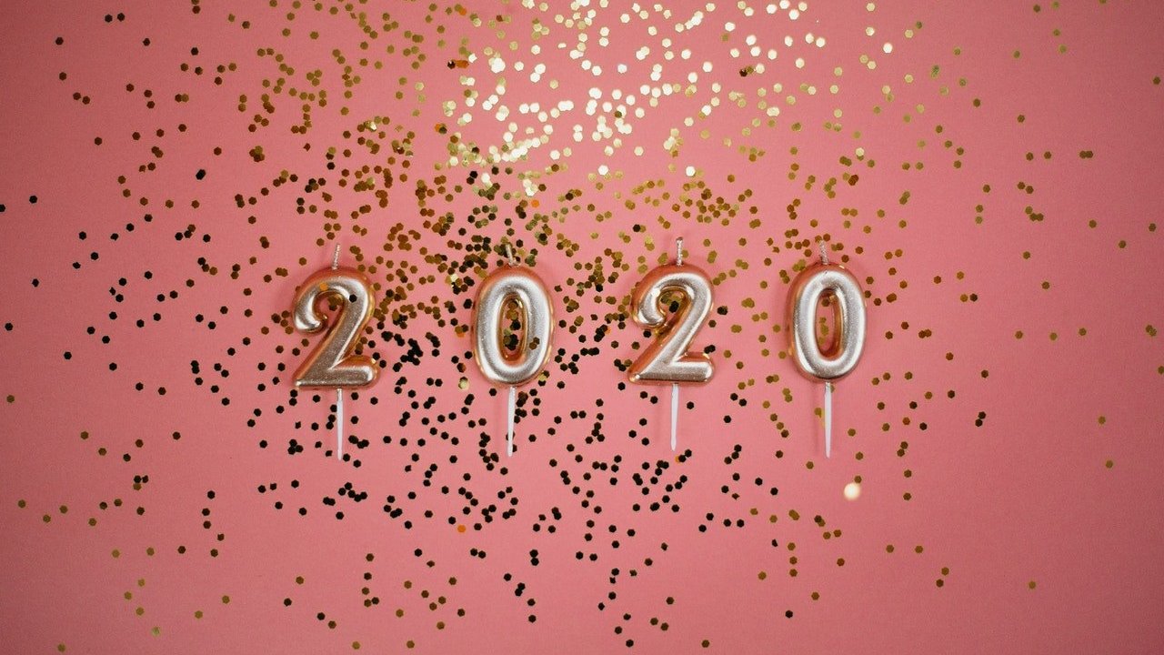 Fundo rosa com brilhos dourados espalhados, e quatro velas, cada uma com um número, escrevendo 2020.