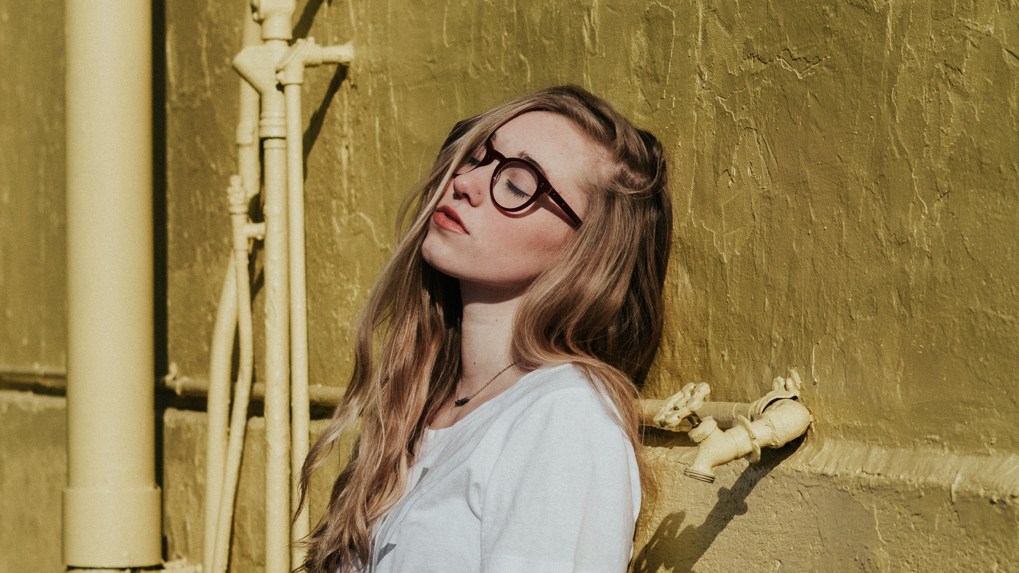 Joanna Nix. Mulher de óculos encostada em uma parede com os olhos fechados.
