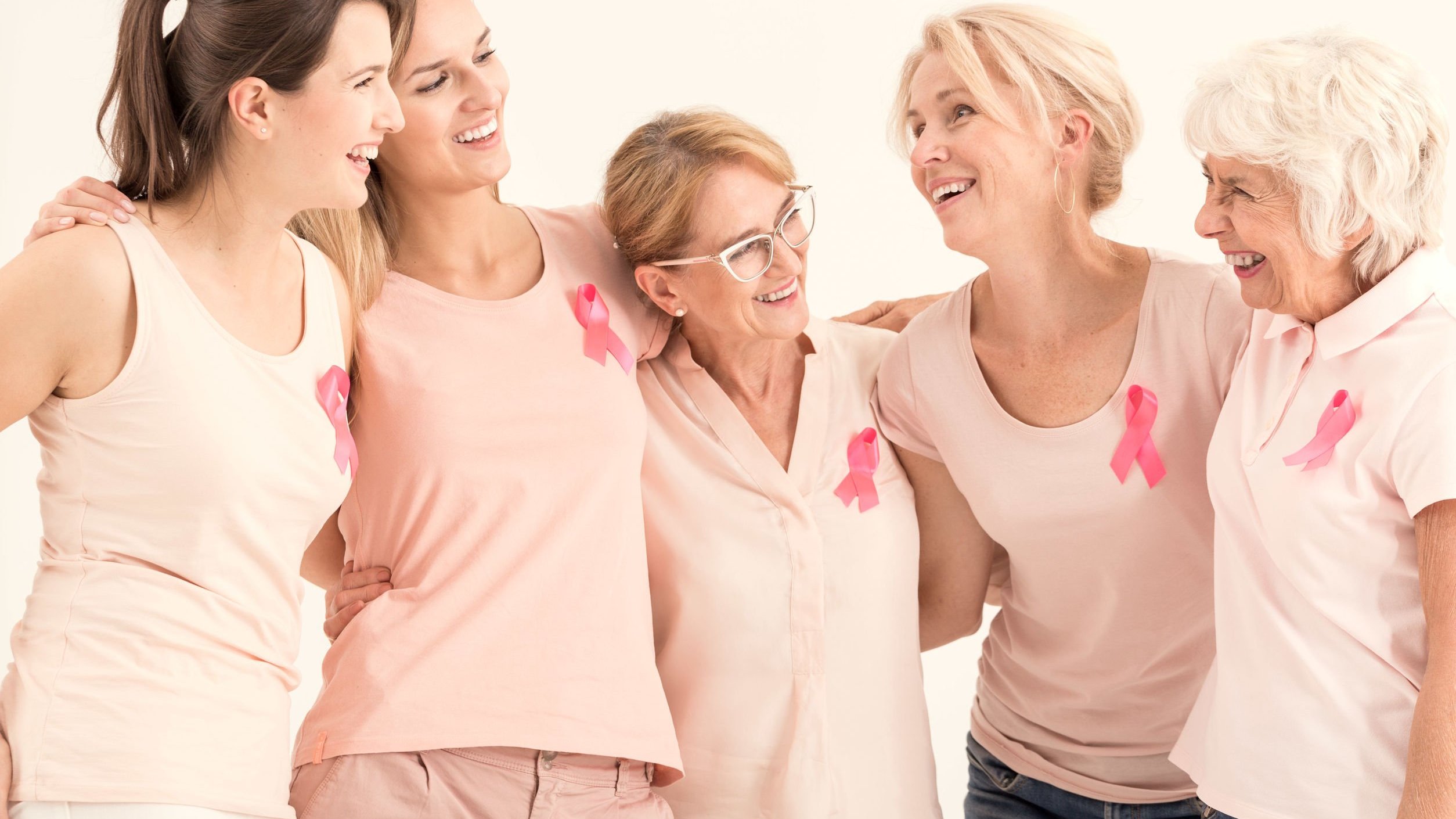 Mulheres sorrindo uma ao lado da outra usando fita rosa na camiseta representando o Outubro Rosa