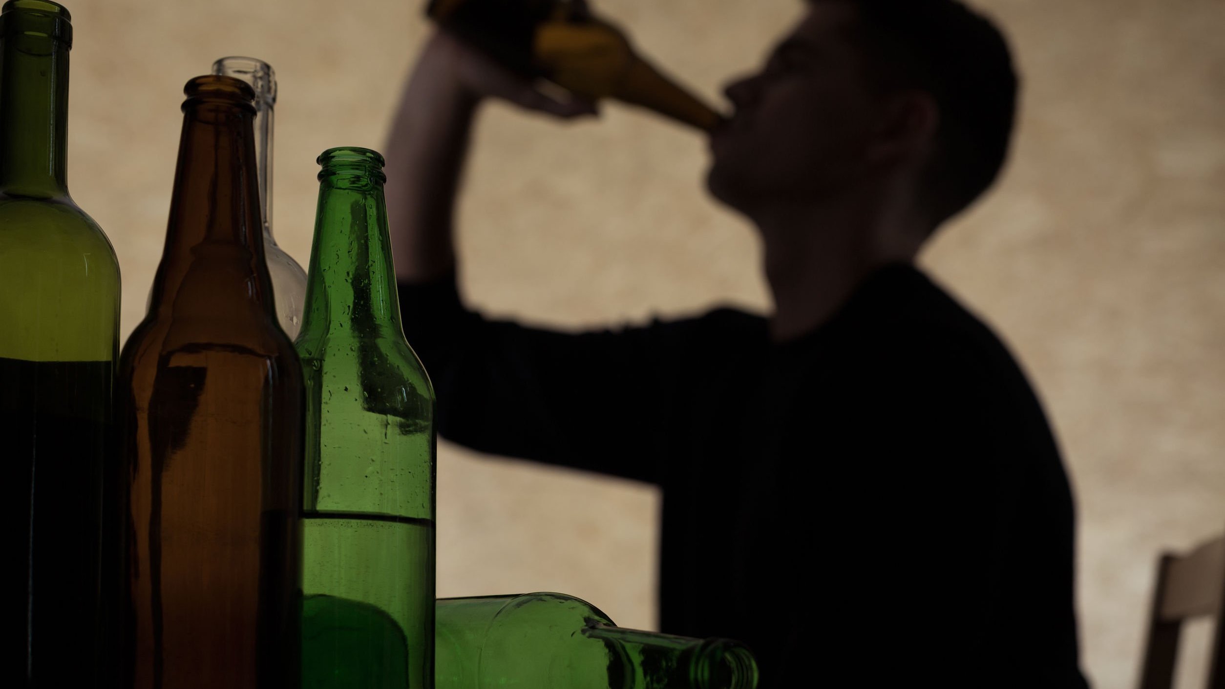 Sombra de um homem tomando bebida e algumas garrafas abertas a sua frente