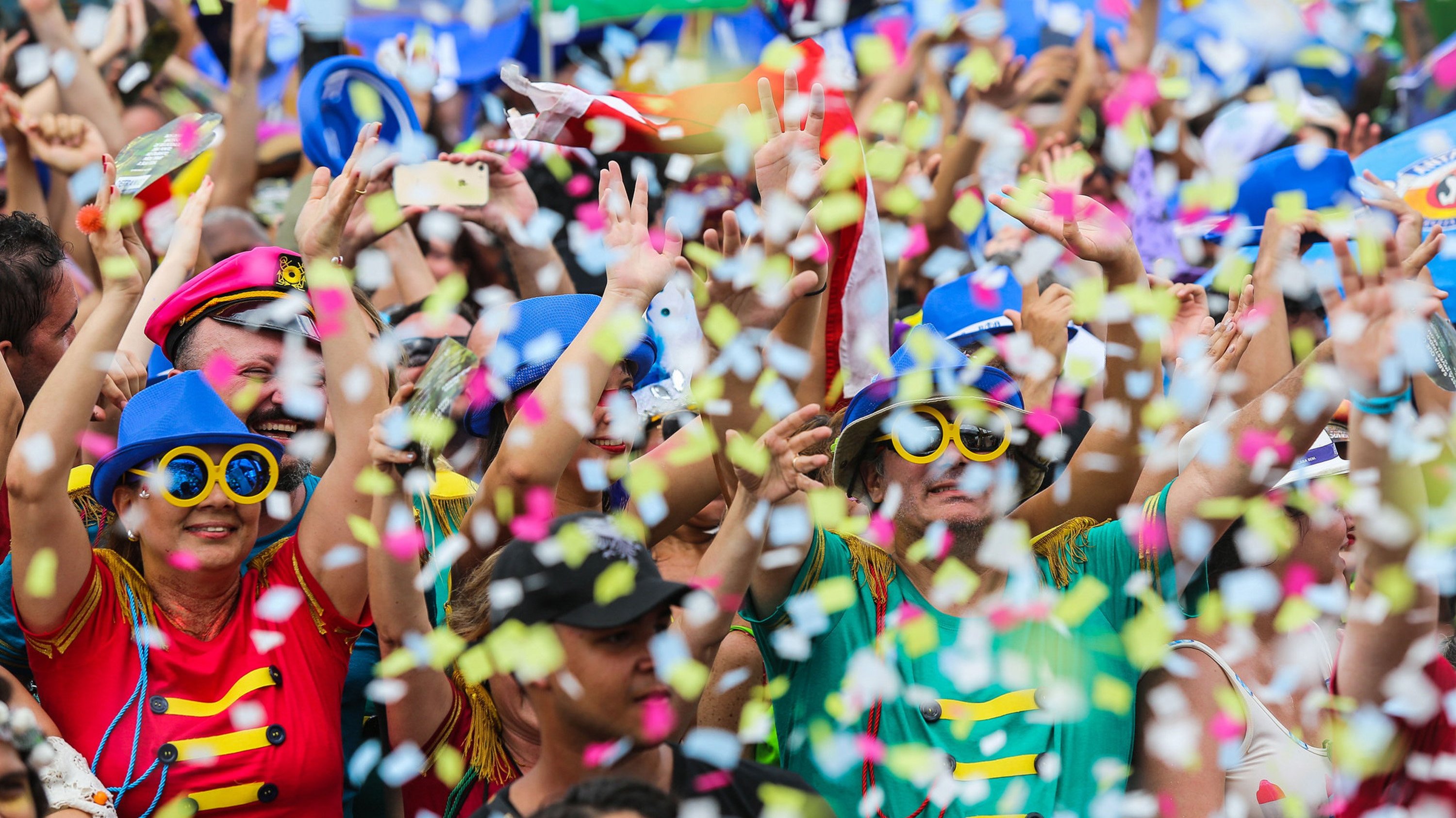 Pessoas comemorando o Carnaval em bloco, com fantasias e confete.