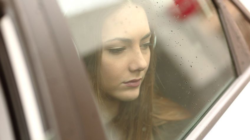 Menina triste olhando pela janela de carro